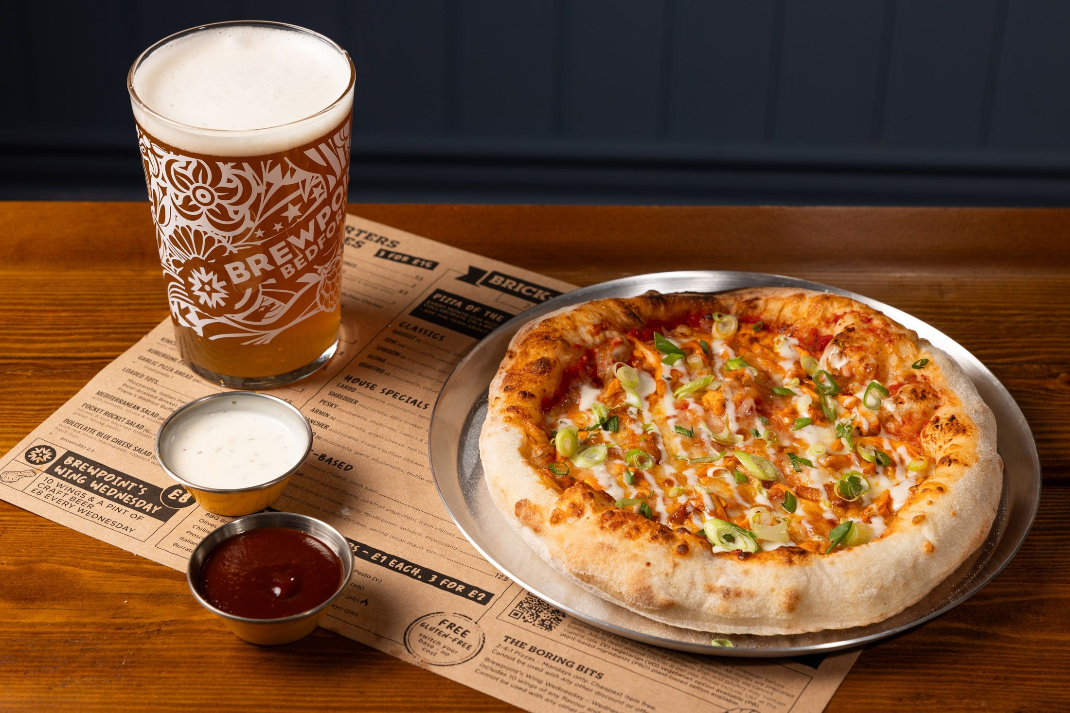 Pizza and Beer on a table with a bbq sauce next to it